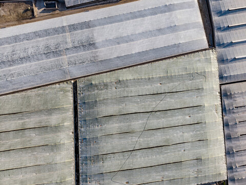 Close vertical drone shot showing detailed textures, structural beams, and weathered surfaces of greenhouse plastic covers.