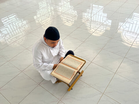 Man Reading Quran on Wooden Stand in Mosque