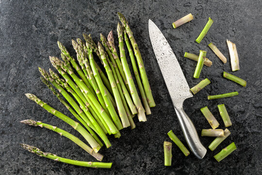Fresh asparagus and knife on a black stone table.