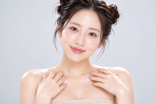 両手を鎖骨に添えて微笑む肌とツインお団子ヘアが美しい女性の美容ポートレート
