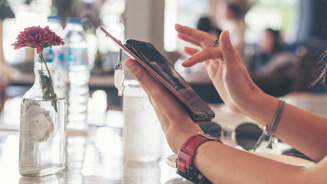 Close-up of Woman hand uses smartphone for mobile communication, during relaxation at restaurant cafe table. Digital lifestyle and internet connection concept