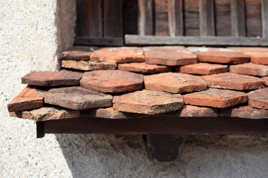 Clay roof tiles layered on a wooden awning. Red and brown hues of old clay tiles. Vintage shingles with irregular hexagonal shapes and chipped edges. Lucerne, Switzerland. Selective focus.