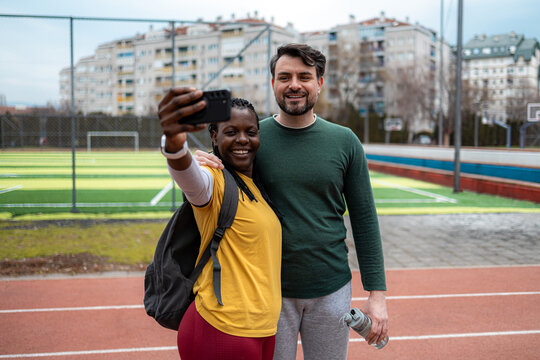 Friends take a selfie at a sports field after exercising on a cloudy day