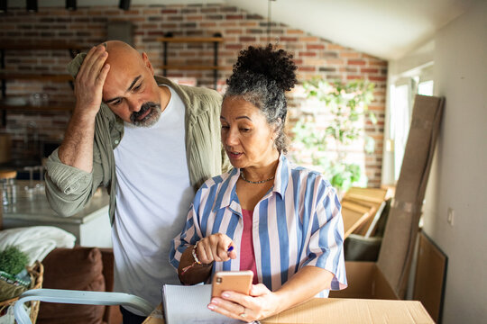 Couple checking phone and notes while unpacking at home
