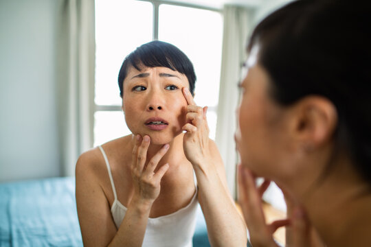 Woman checking eye area in mirror at home