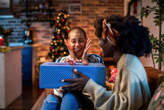 Woman surprising friend with a christmas gift at home
