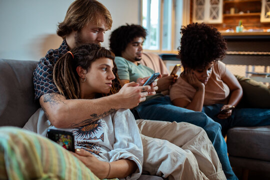 Couple sharing a phone while friends scroll on couch