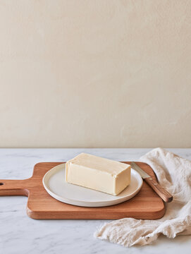 block of butter resting on a small white plate over a wooden cutting board.