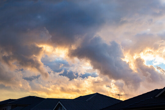 Clouds above rooftops silhouetted against sunset sky