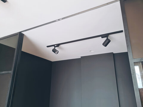 Modern LED track lighting system with two black spotlights on ceiling in built-in wardrobe closet