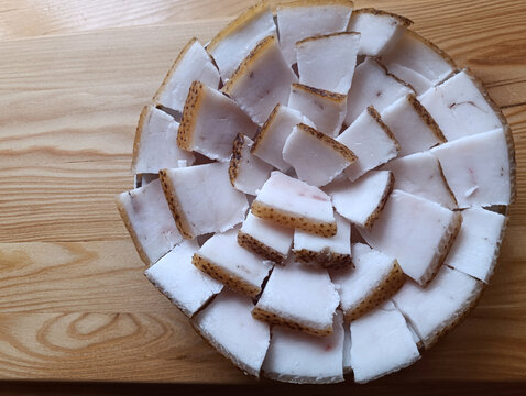 traditional salo, pork fatback with brown skin arranged on a wooden plate, close-up of white fat, rustic wooden table, eastern european cuisine, fresh meat texture and traditional food