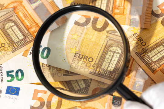 hand holding magnifying glass inspecting euro banknotes. Financial investigation tracing auditing concept