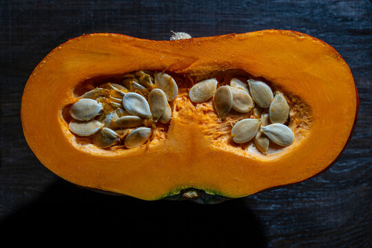 Half of ripe pumpkin with seeds inside on table background. Fresh organic pumpkin cut in half with healthy seeds inside, closeup shot on dark wooden texture