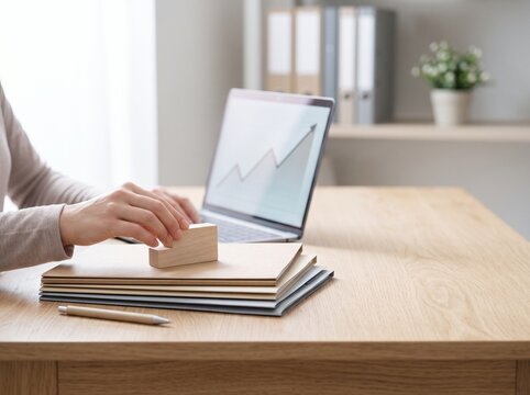 Close up of hands typing on laptop with growth chart on screen and wooden block on documents