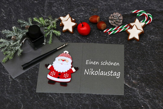 Gru&szlig;karte zum Nikolaustag mit Weihnachtsmann, Federhalter, Tinte und traditioneller Dekoration auf dunklem Hintergrund.
