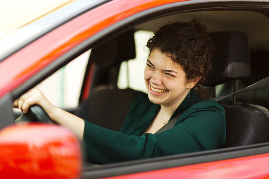 Happy young woman laughing while driving a red car