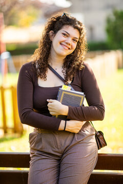 Smiling young woman holding a book in sunny outdoor setting