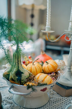 striped orange pumpkins and green gourd in white colander on lace table, cozy autumn harvest decoration featuring seasonal squash near vintage candlestick