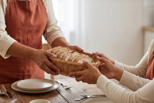 Hands passing a basket of bread across a kitchen table