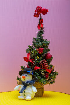 snowman crocheted from yarn, placed on a colorful background next to a Christmas tree