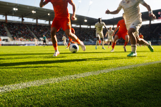 Low angle close up of football players competing for the ball on a sunlit pitch during a professional soccer match