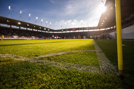 Low angle view of a football stadium with green grass, goalpost, floodlights and bright evening sunlight before a soccer match