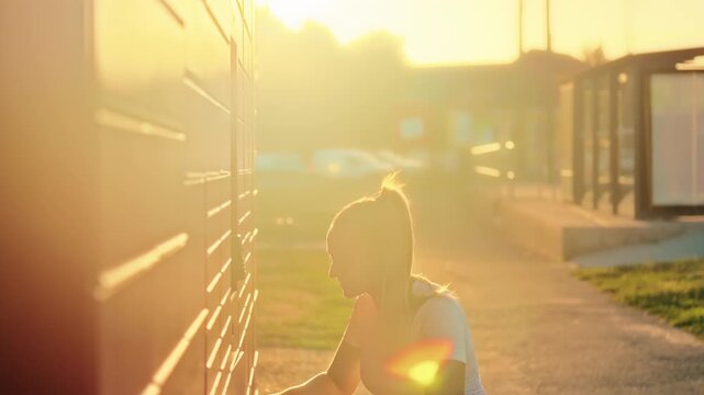 Woman retrieving a package from a self-service parcel locker with beautiful golden hour sunlight