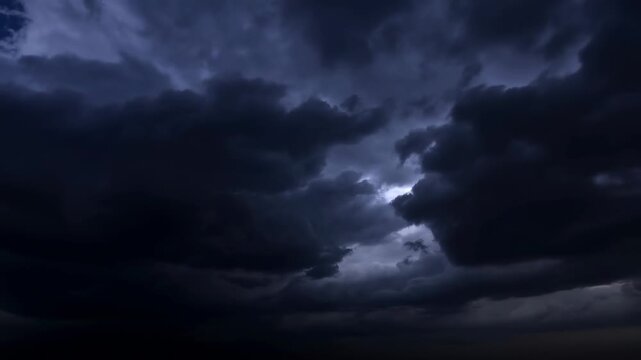 Dark thunderstorm clouds roll across the nighttime sky as lightning flashes through the storm system. Weather reporting, severe weather education, and storm documentary.