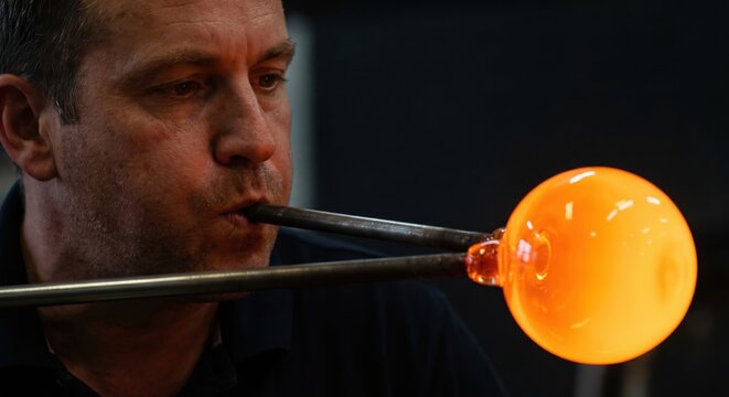 Glassblower carefully shaping a glowing orb of molten glass on a blowpipe