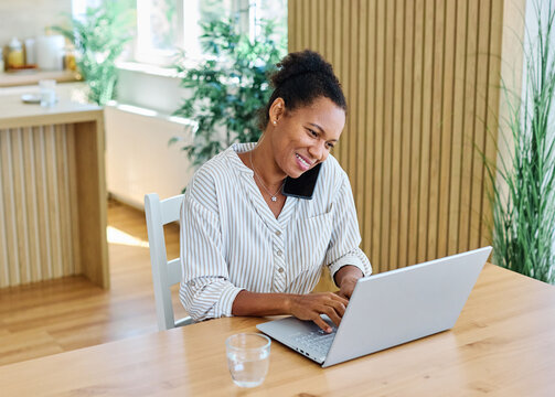 Portrait of a young black woman using a smartphone and laptop at home office