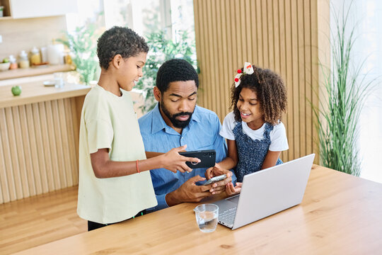 Portrait of ayoung businessman working on laptop from home distracted by surrounding noisy children. Fatherhood, childhood, family, freelance job, home office concept