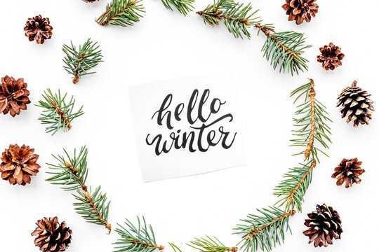 Hello winter hand lettering. Winter pattern with spruce branches and pinecones on white background top view