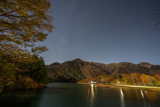 Starry night sky above autumn mountains and a quiet lakeside lodge