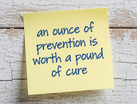 Yellow sticky note with handwritten wise quote on old white wooden wall. Text says ounce of prevention worth pound of cure. Concept of health care, proactive lifestyle, wellness advice for daily