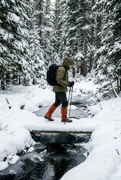 Hiker with backpack crossing a snowy forest stream during a quiet winter adventure for travel editorial.