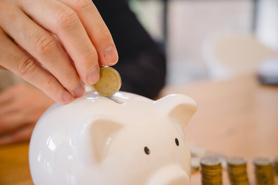 A man is putting coins into a piggy bank. Concept of saving money and being financially responsible. personal finance investment banking wealth financial planning