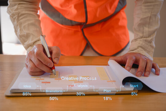 Engineer wearing safety vest writing on documents or checklists safety check at work desk. Concept of construction planning, project management, engineering analysis and professional workflow.