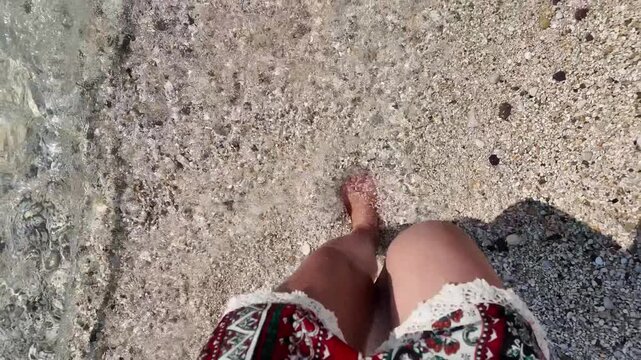 Unrecognizable woman walking barefoot on a pebble beach near the sea