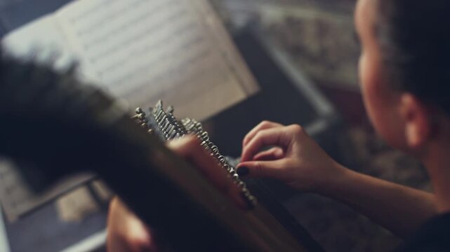 Zither player plucking strings close up. Woman reading sheet music dark room.