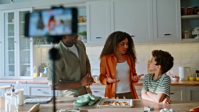 Mother talking smartphone camera kitchen. Mixed race family filming baking vlog.