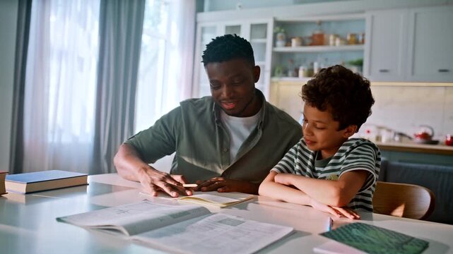 Son studying father kitchen table. Multiethnic family school homework together.