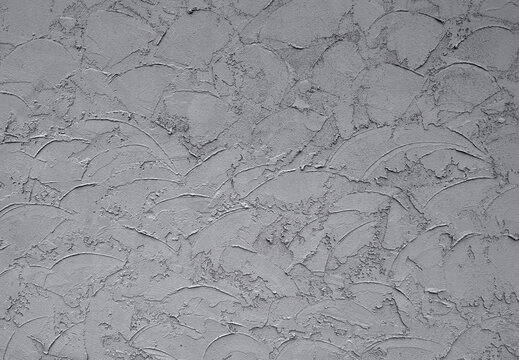 Gray painted skip trowel stucco wall with rough porous texture, overlapping semicircular trowel arcs in a haphazard pattern, and contrasting smooth and coarse areas across the uneven plaster surface