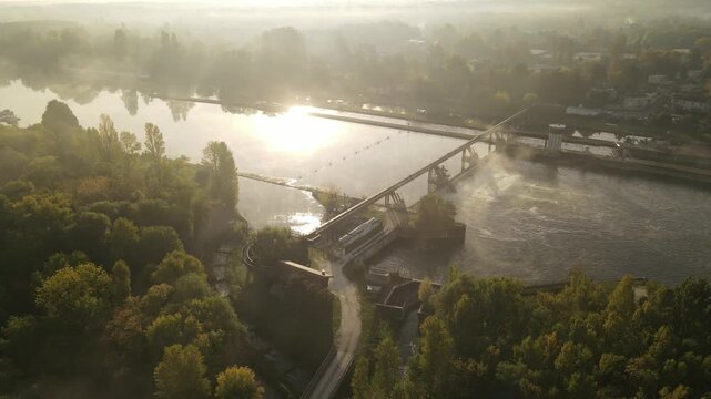Aerial view of a river and dam with a small hydro-electric power station, sunlight streaming through trees in the morning, Chartrettes, France