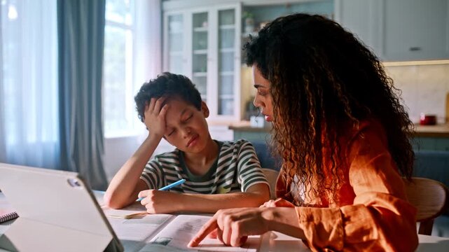 Woman explaining textbook exercise frustrated son kitchen. Homework help tablet.