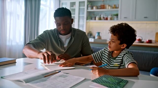 Smiling dad explaining lesson kitchen. African american boy writing homework.