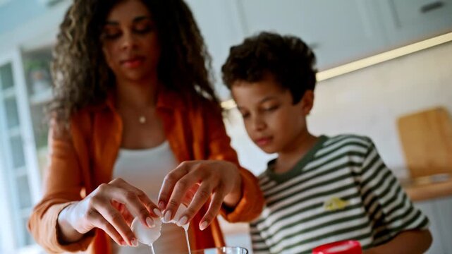 Kid pouring milk glass bowl. Woman breaking eggs cozy home kitchen breakfast.