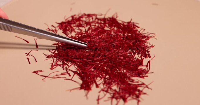 Woman putting crocus stigmas (saffron) with tweezers onto beige background, closeup