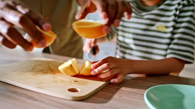 Child slicing oranges kitchen counter. Single father son high five celebration.