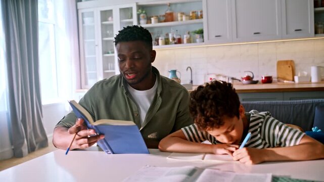 Father reading book helping son homework. Dad tutoring young boy kitchen table.