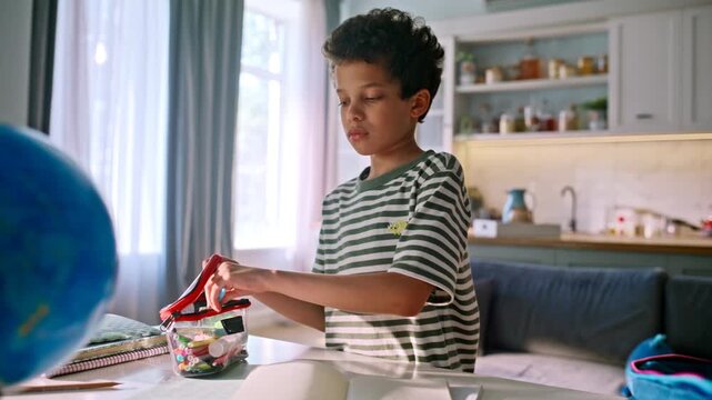 Schoolboy packing backpack home kitchen. Pupil preparing pencil case school bag.